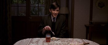 Movie still from “An Education” (2009), directed by Lone Scherfig – A young man sitting at a table with a plate of food; Medium shot, Over the shoulder angle
