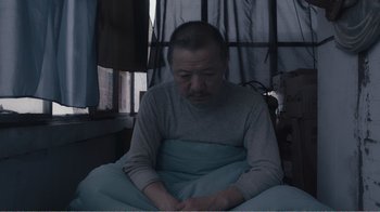 Movie still from “An Elephant Sitting Still” (2018), directed by Bo Hu – An older man sitting in a bed under a blanket; Medium shot, Low angle