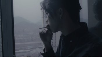 Movie still from “An Elephant Sitting Still” (2018), directed by Bo Hu – A man smoking a cigarette in front of a large window; Close Up shot, Over the shoulder angle