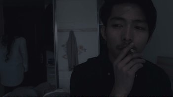 Movie still from “An Elephant Sitting Still” (2018), directed by Bo Hu – A man smoking a cigarette in a dark room; Close Up shot, Overhead angle