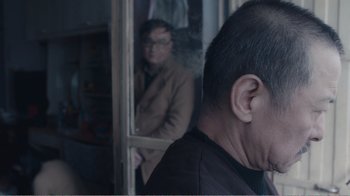 Movie still from “An Elephant Sitting Still” (2018), directed by Bo Hu – A man standing in front of a window with a woman behind him; Close Up shot, Over the shoulder angle