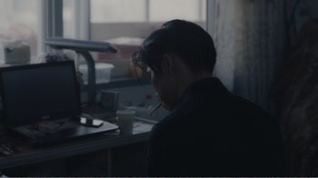Movie still from “An Elephant Sitting Still” (2018), directed by Bo Hu – A man sitting in front of a computer with a cigarette in his mouth; Medium shot, Over the shoulder angle