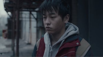 Movie still from “An Elephant Sitting Still” (2018), directed by Bo Hu – A young man in a red jacket is looking down; Close Up shot, Over the shoulder angle