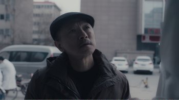 Movie still from “An Elephant Sitting Still” (2018), directed by Bo Hu – A man with a hat standing in the street; Close Up shot, Low angle