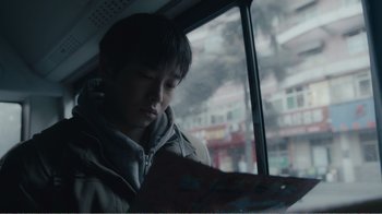 Movie still from “An Elephant Sitting Still” (2018), directed by Bo Hu – A man sitting on a bus looking at a book; Close Up shot, Over the shoulder angle