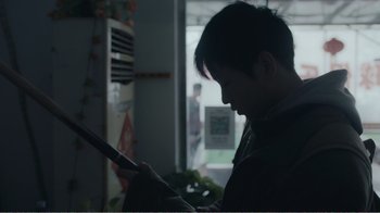 Movie still from “An Elephant Sitting Still” (2018), directed by Bo Hu – A man looking at a tablet in a kitchen; Close Up shot, Over the shoulder angle