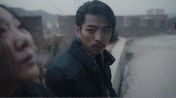 Movie still from “An Elephant Sitting Still” (2018), directed by Bo Hu – A man in a black jacket is standing outside; Close Up shot, Over the shoulder angle