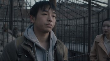 Movie still from “An Elephant Sitting Still” (2018), directed by Bo Hu – A young man standing in front of a metal fence; Close Up shot, High angle