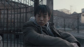 Movie still from “An Elephant Sitting Still” (2018), directed by Bo Hu – A man sitting on top of a metal fence; Close Up shot, High angle