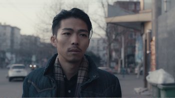 Movie still from “An Elephant Sitting Still” (2018), directed by Bo Hu – A man with a beard is standing on the street; Close Up shot, Low angle