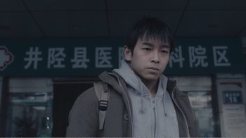 Movie still from “An Elephant Sitting Still” (2018), directed by Bo Hu – A young man standing in front of an asian sign; Close Up shot, Low angle