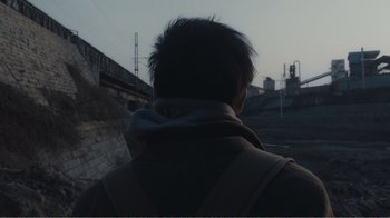 Movie still from “An Elephant Sitting Still” (2018), directed by Bo Hu – A man wearing a hoodie looking at a bridge; Close Up shot, Over the shoulder angle