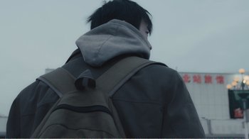 Movie still from “An Elephant Sitting Still” (2018), directed by Bo Hu – A person with a backpack walking on a cloudy day; Extreme Close Up shot, Low angle