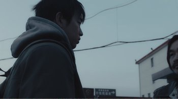 Movie still from “An Elephant Sitting Still” (2018), directed by Bo Hu – A young man standing in front of a street sign; Close Up shot, Low angle