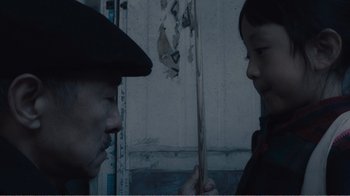 Movie still from “An Elephant Sitting Still” (2018), directed by Bo Hu – A man and a child face each other in front of a building; Medium shot, Over the shoulder angle