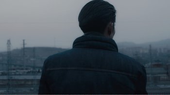 Movie still from “An Elephant Sitting Still” (2018), directed by Bo Hu – A man wearing a black jacket looking out a window; Close Up shot, Over the shoulder angle