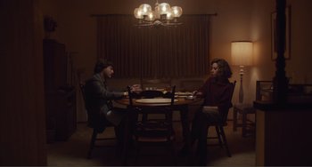 Movie still from “An Evening with Beverly Luff Linn” (2018), directed by Jim Hosking – Two people are sitting at a table in a dimly - lit room; Wide shot, High angle