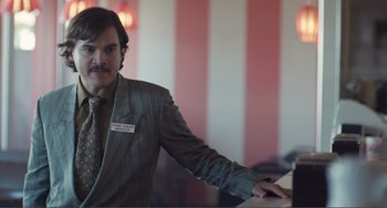 Movie still from “An Evening with Beverly Luff Linn” (2018), directed by Jim Hosking – A man standing at a bar wearing a suit and tie; Medium shot, Low angle