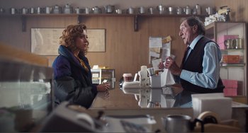 Movie still from “An Evening with Beverly Luff Linn” (2018), directed by Jim Hosking – Two people are sitting at a table with cups; Medium shot, Over the shoulder angle