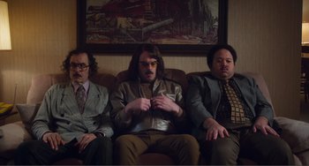 Movie still from “An Evening with Beverly Luff Linn” (2018), directed by Jim Hosking – A group of men sitting in a row on top of a couch; Wide shot, Low angle