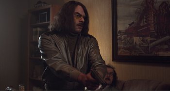 Movie still from “An Evening with Beverly Luff Linn” (2018), directed by Jim Hosking – A man with long hair and glasses holding a nintendo wii game controller; Medium shot, Over the shoulder angle