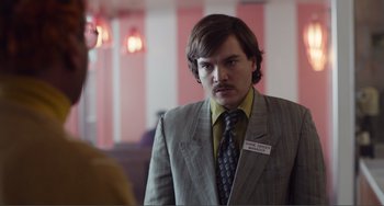 Movie still from “An Evening with Beverly Luff Linn” (2018), directed by Jim Hosking – A man in a suit and tie standing in a room; Close Up shot, Over the shoulder angle