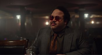 Movie still from “An Evening with Beverly Luff Linn” (2018), directed by Jim Hosking – A man in a suit and sunglasses sitting at a table in a restaurant; Medium shot, Low angle