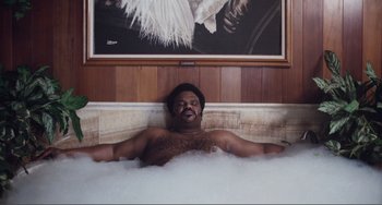 Movie still from “An Evening with Beverly Luff Linn” (2018), directed by Jim Hosking – A man laying in a bath tub in front of a painting; Medium shot, Low angle