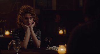 Movie still from “An Evening with Beverly Luff Linn” (2018), directed by Jim Hosking – A woman sitting at a table with a glass of wine in front of a candle; Medium shot, Over the shoulder angle