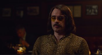 Movie still from “An Evening with Beverly Luff Linn” (2018), directed by Jim Hosking – A man with long brown hair and sunglasses; Medium shot, Over the shoulder angle