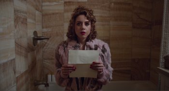 Movie still from “An Evening with Beverly Luff Linn” (2018), directed by Jim Hosking – A woman holding a piece of paper while standing in front of a mirror; Medium shot, High angle