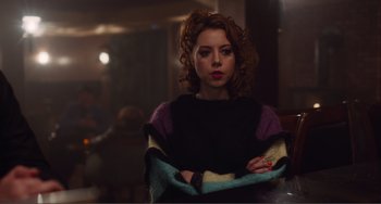 Movie still from “An Evening with Beverly Luff Linn” (2018), directed by Jim Hosking – A woman in a black and purple sweater holding a towel; Medium shot, Over the shoulder angle