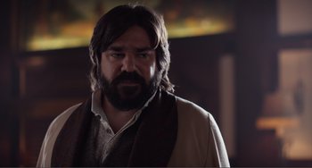 Movie still from “An Evening with Beverly Luff Linn” (2018), directed by Jim Hosking – A man with long hair and a beard wearing a vest; Close Up shot, Over the shoulder angle