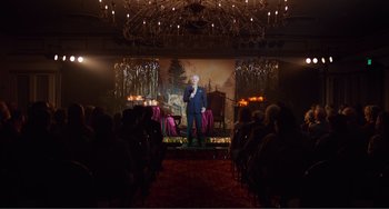 Movie still from “An Evening with Beverly Luff Linn” (2018), directed by Jim Hosking – A man standing on a stage in front of an audience; Wide shot, Over the shoulder angle