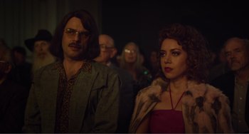 Movie still from “An Evening with Beverly Luff Linn” (2018), directed by Jim Hosking – A man and a woman standing next to each other in a room; Medium shot, Over the shoulder angle