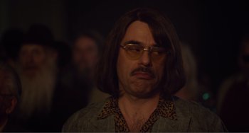Movie still from “An Evening with Beverly Luff Linn” (2018), directed by Jim Hosking – A man with long brown hair and glasses; Close Up shot, Over the shoulder angle