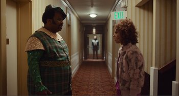 Movie still from “An Evening with Beverly Luff Linn” (2018), directed by Jim Hosking – Two people standing in a hotel hallway talking to each other; Medium shot, Over the shoulder angle