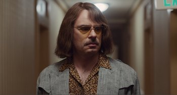 Movie still from “An Evening with Beverly Luff Linn” (2018), directed by Jim Hosking – A man with long brown hair wearing sunglasses and a leopard print shirt; Close Up shot, Over the shoulder angle