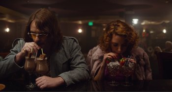 Movie still from “An Evening with Beverly Luff Linn” (2018), directed by Jim Hosking – Two people sitting at a table with a drink; Medium shot, Over the shoulder angle