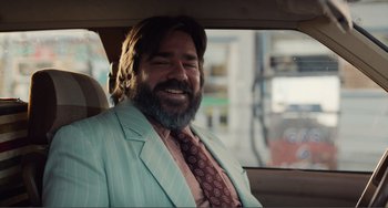 Movie still from “An Evening with Beverly Luff Linn” (2018), directed by Jim Hosking – A man in a suit and tie sitting in the back of a car; Medium shot, Over the shoulder angle