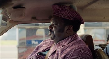 Movie still from “An Evening with Beverly Luff Linn” (2018), directed by Jim Hosking – A man in a plaid jacket sitting in the back of a car; Close Up shot, Over the shoulder angle