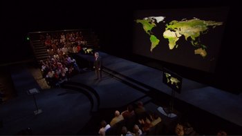 Movie still from “An Inconvenient Truth” (2006), directed by Davis Guggenheim – A man standing in front of an audience in front of a projection screen; Extreme Wide shot, High angle