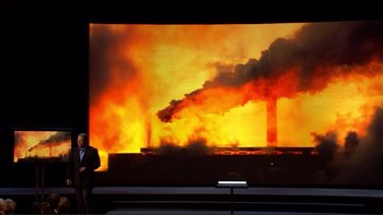 Movie still from “An Inconvenient Truth” (2006), directed by Davis Guggenheim – A man standing in front of a large screen with smoke coming out of a factory; Extreme Wide shot, Over the shoulder angle
