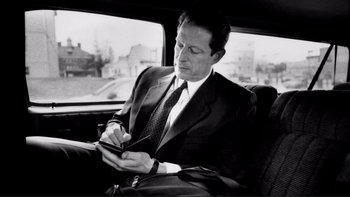 Movie still from “An Inconvenient Truth” (2006), directed by Davis Guggenheim – A black and white photo of a man in a suit writing on a piece of paper while sitting in a car; Close Up shot, High angle
