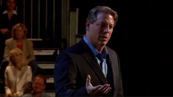 Movie still from “An Inconvenient Truth” (2006), directed by Davis Guggenheim – A man wearing a suit and tie talking to a crowd of onlookers; Medium shot, Over the shoulder angle