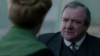 Movie still from “An Inspector Calls” (2015), directed by Raymond Pak-Ming Wong – An older man wearing a suit and tie talking to a woman; Close Up shot, Over the shoulder angle