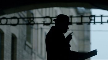 Movie still from “An Inspector Calls” (2015), directed by Raymond Pak-Ming Wong – A man smoking a cigarette while standing in front of a building; Medium shot, Low angle