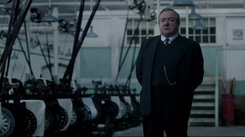 Movie still from “An Inspector Calls” (2015), directed by Raymond Pak-Ming Wong – A man in a suit standing in front of machinery; Medium shot, Low angle