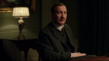Movie still from “An Inspector Calls” (2015), directed by Raymond Pak-Ming Wong – A man sitting at a table wearing a suit and tie; Close Up shot, Low angle
