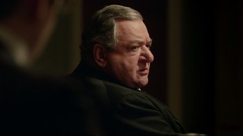 Movie still from “An Inspector Calls” (2015), directed by Raymond Pak-Ming Wong – An older man in a black jacket looking at the camera; Close Up shot, Over the shoulder angle